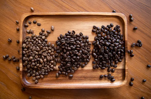 Light, medium and dark roasted coffee beans side by side on a wooden tray