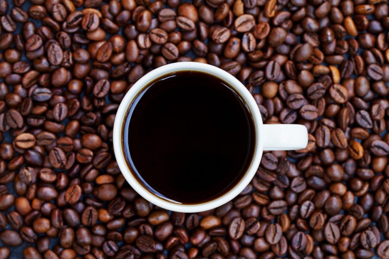 Black Coffee in White Cup on Freshly Roasted Coffee Beans Background. Top View. Copy Space.